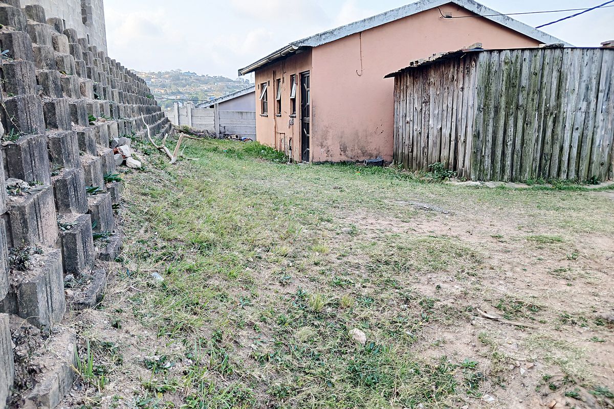 Rear exterior view showing a concrete retaining wall, a small outbuilding with a pitched roof, and a timber fence enclosure.