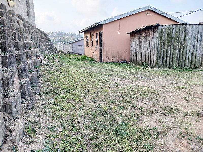 Rear exterior view showing a concrete retaining wall, a small outbuilding with a pitched roof, and a timber fence enclosure.