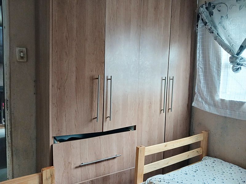 Bedroom featuring a built-in wooden wardrobe with a damaged drawer and visible wall wear, requiring minor repairs and cosmetic updates.