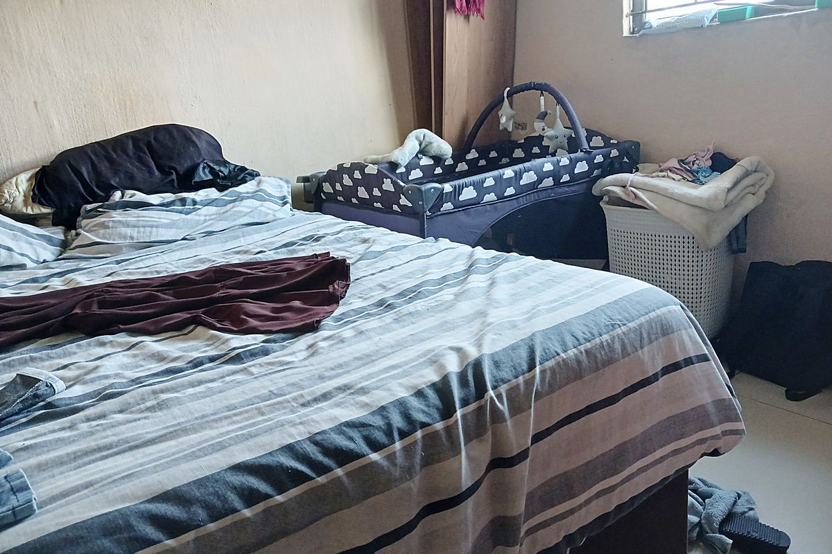 A bedroom featuring tiled flooring and a window with security bars, currently showing signs of wear on the wall surfaces.