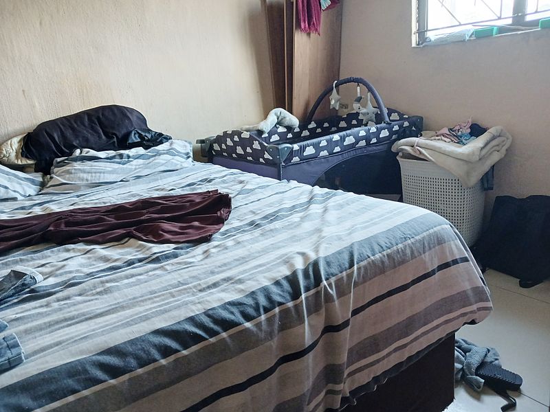 A bedroom featuring tiled flooring and a window with security bars, currently showing signs of wear on the wall surfaces.