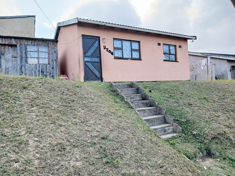 Front elevation of a single-story residential house featuring a concrete staircase entrance, security bars on windows, and an adjacent corrugated metal storage structure.
