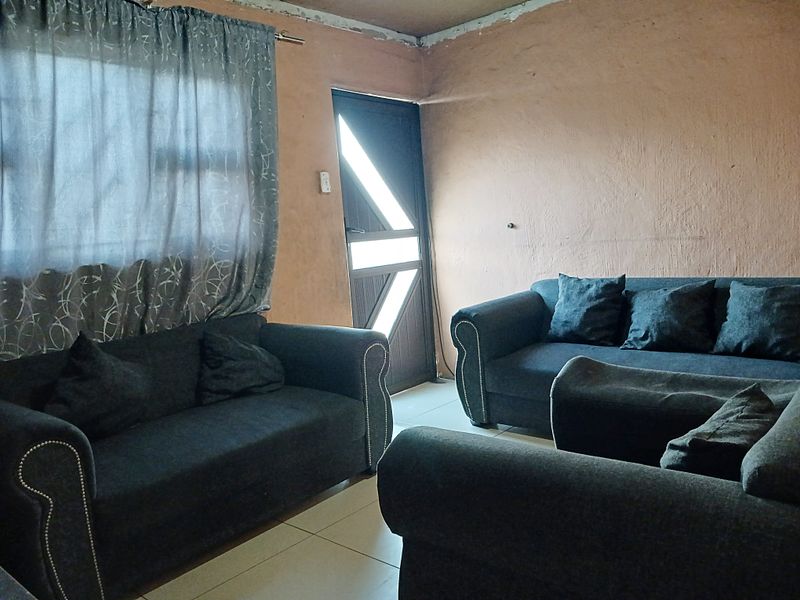 A living room area featuring tiled flooring and an external door, currently requiring cosmetic updates to the wall finishes and ceiling junctions.