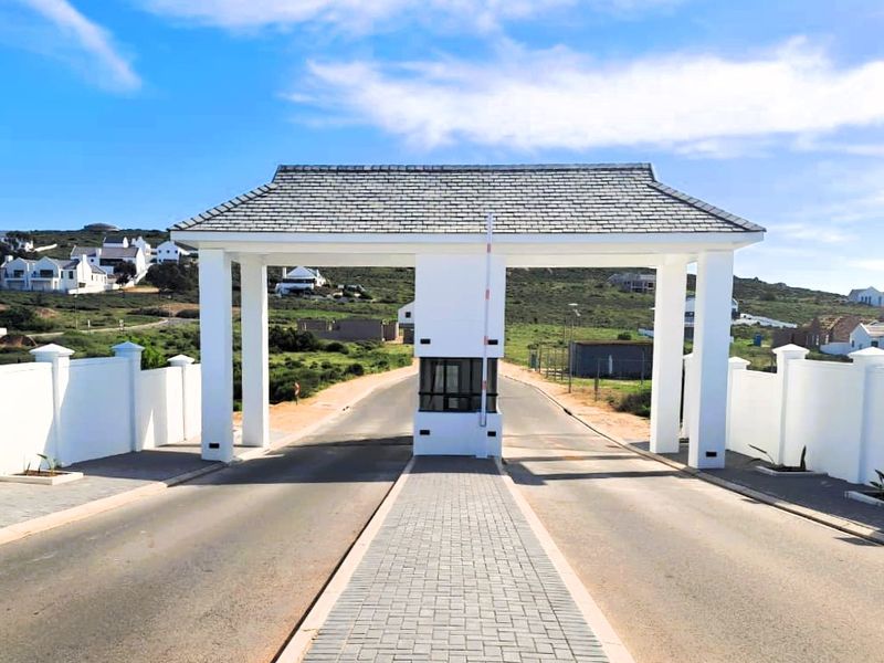 A well-maintained residential estate entrance featuring a modern security gatehouse, paved driveway, and perimeter walling.
