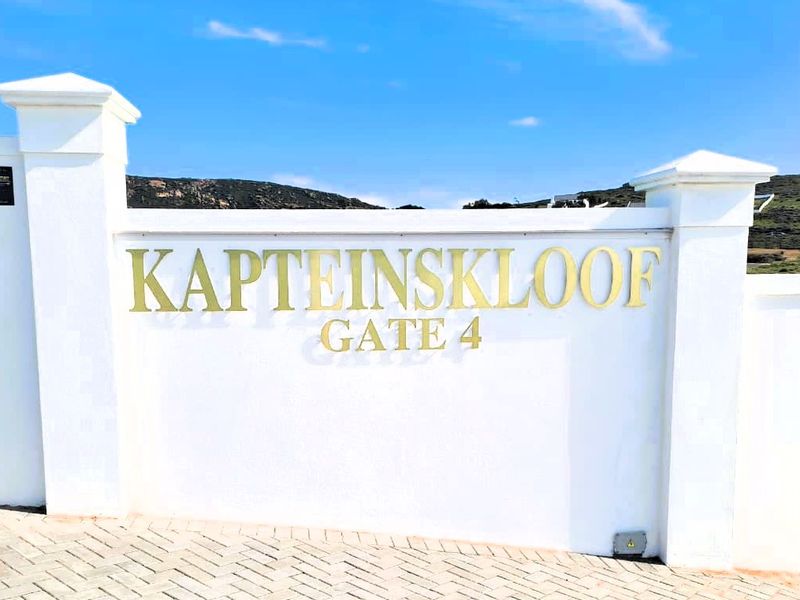 A clear view of the entrance signage for Kapteinskloof Gate 4, featuring a well-maintained white boundary wall and paved driveway.