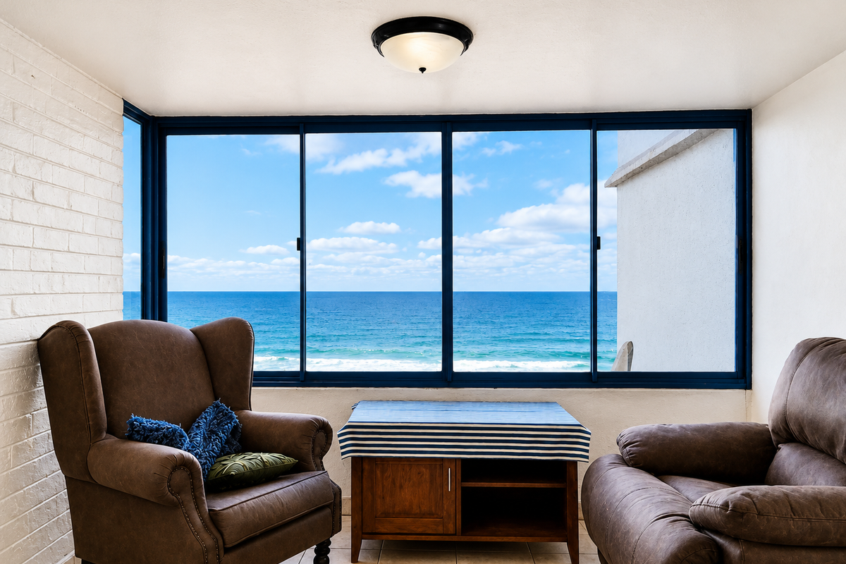 A bright enclosed balcony or sunroom featuring tiled flooring, painted brick accents, and expansive windows offering direct, unobstructed ocean views.