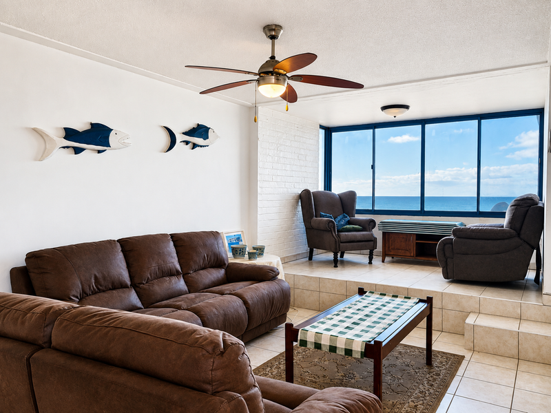 Spacious living area featuring a raised platform, tiled flooring, ceiling fan, and large windows offering expansive ocean views.
