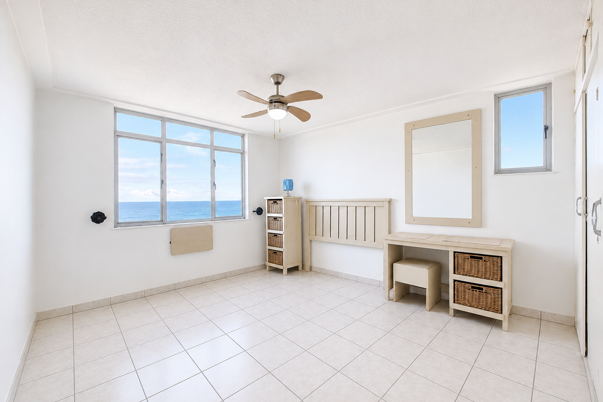 Bright bedroom featuring tiled flooring, a ceiling fan, and large windows offering expansive ocean views, providing a light and airy living space.