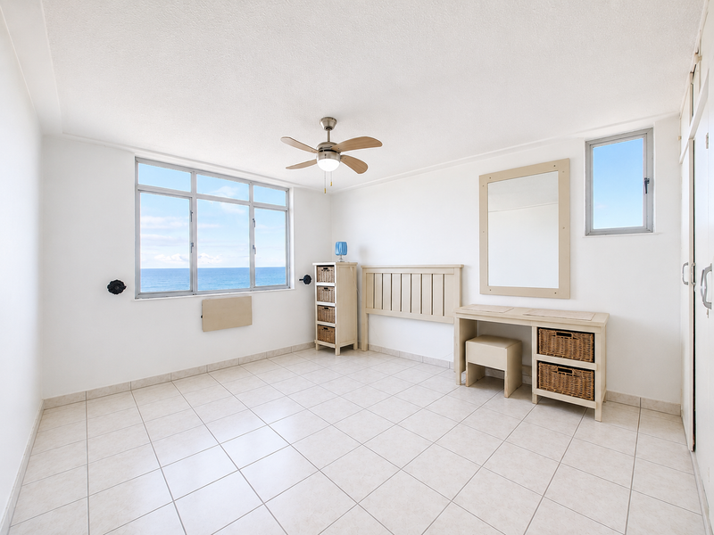 Bright bedroom featuring tiled flooring, a ceiling fan, and large windows offering expansive ocean views, providing a light and airy living space.