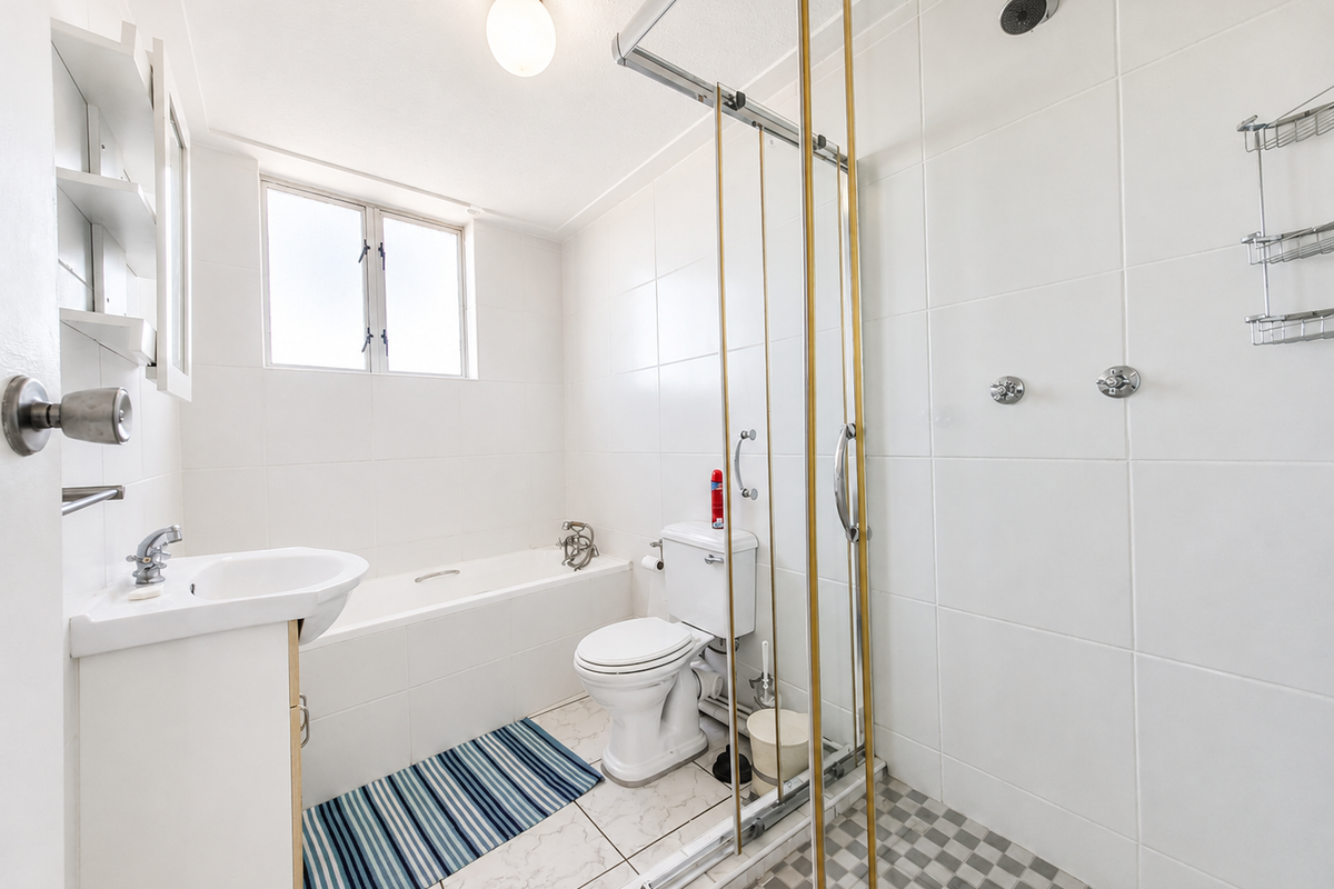 A functional bathroom featuring a combined bathtub and shower enclosure, pedestal basin, and white tiled finishes throughout.