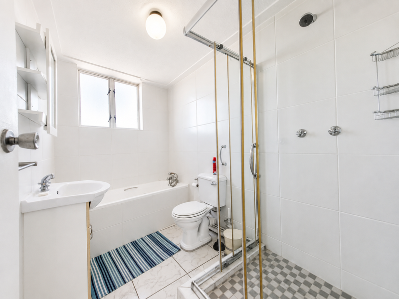 A functional bathroom featuring a combined bathtub and shower enclosure, pedestal basin, and white tiled finishes throughout.