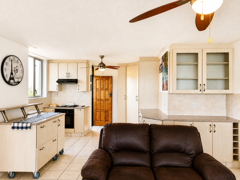 Open-plan kitchen and living area featuring light wood cabinetry, tiled flooring, built-in appliances, and a ceiling fan.