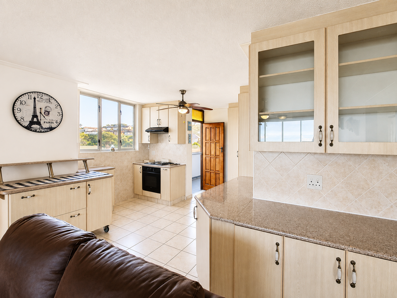 Open-plan kitchen and living area featuring light wood cabinetry, granite countertops, tiled flooring, and a built-in oven with extractor fan.