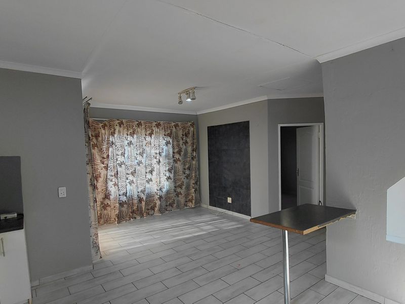 Open plan living and kitchen area featuring tiled flooring, a breakfast bar, and neutral grey wall finishes.