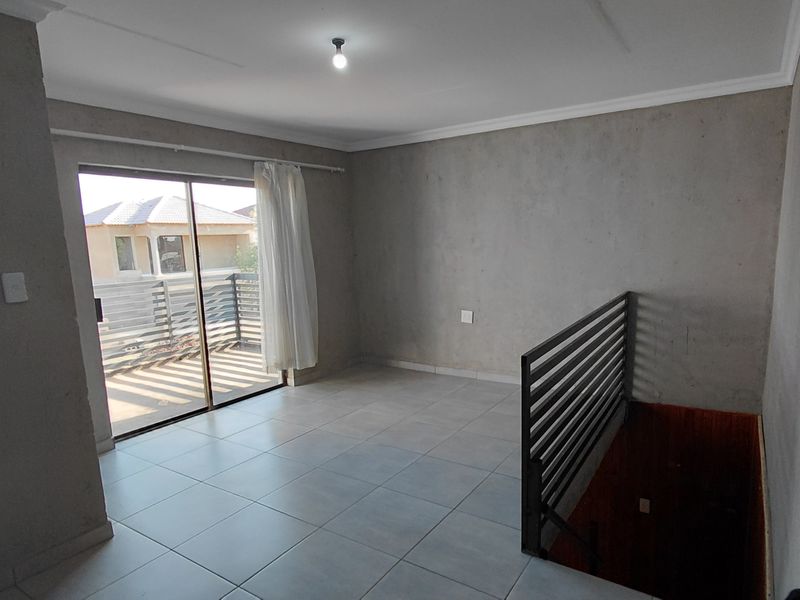An empty, unfinished living area featuring tiled floors, a metal stair railing, and a sliding glass door leading to an outdoor balcony.