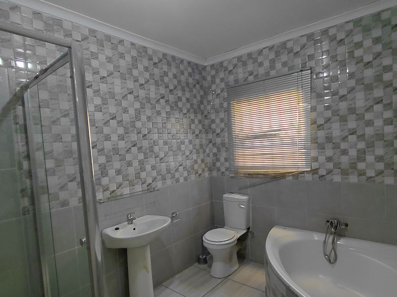 A functional bathroom featuring a corner bathtub, separate shower enclosure, pedestal basin, and toilet with tiled finishes throughout.