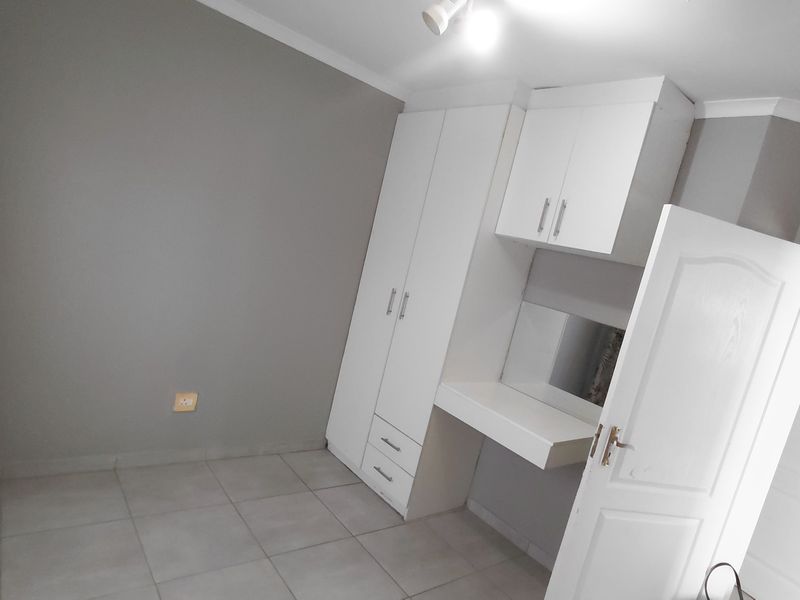A clean, neutral-toned bedroom featuring tiled flooring, built-in white cabinetry, and a matching vanity unit with integrated storage.