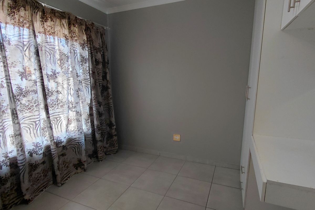 A clean, empty bedroom featuring neutral tiled flooring, built-in cupboards, and a large window with natural light.
