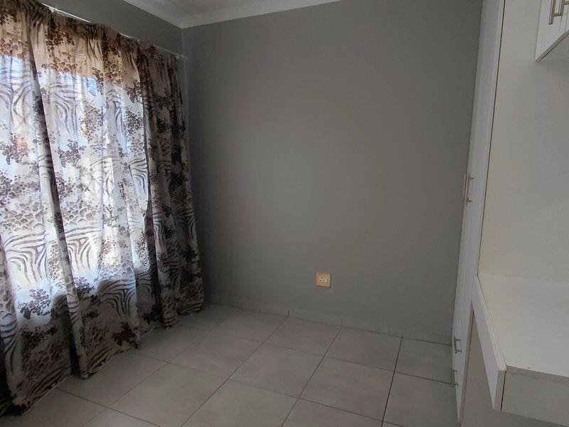 A clean, empty bedroom featuring neutral tiled flooring, built-in cupboards, and a large window with natural light.