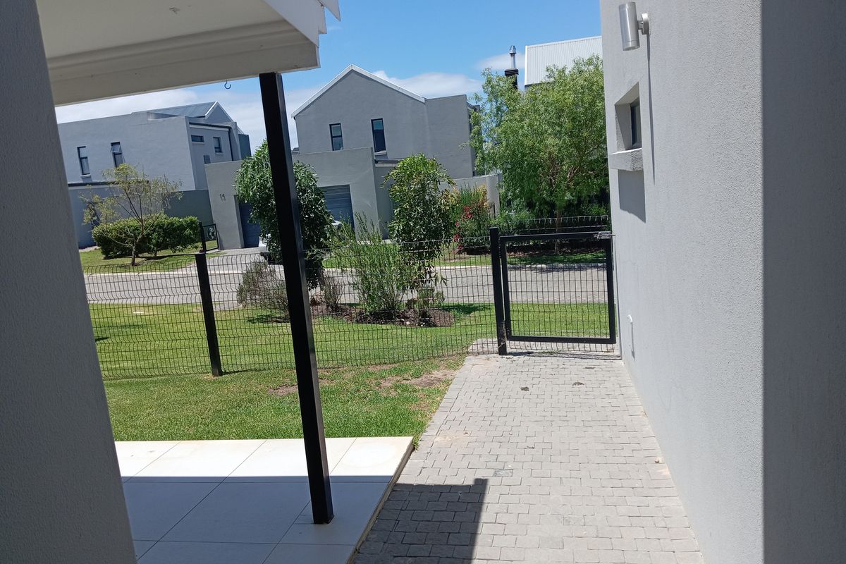 A view of the rear exterior featuring a paved walkway, tiled patio area, and metal fencing leading to the garden.