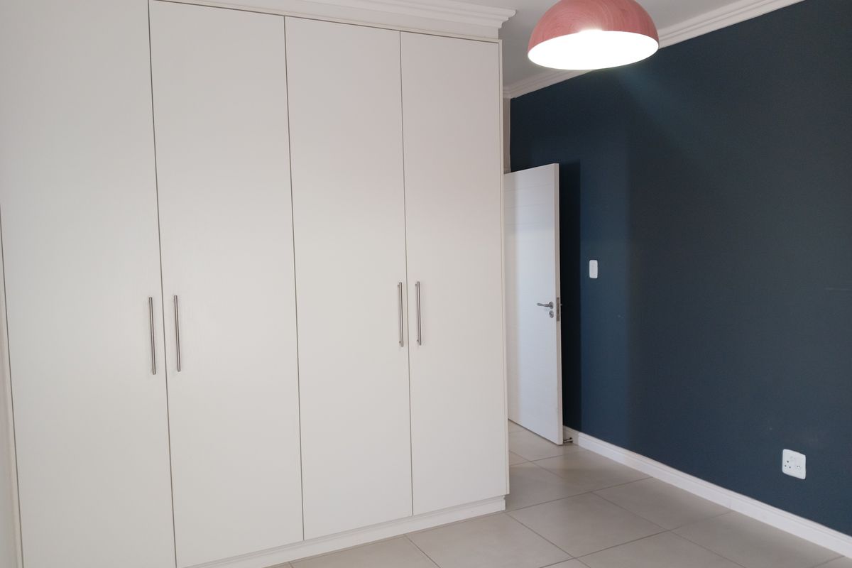 A clean, modern bedroom featuring large white built-in cupboards, neutral tiled flooring, and a dark accent wall, providing a versatile space for personalization.