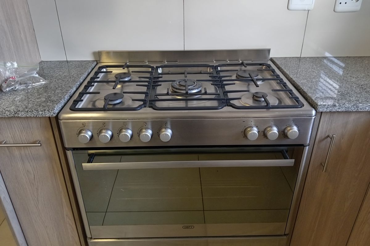 A clean, modern kitchen featuring a stainless steel gas hob and oven set within granite countertops and light wood-finish cabinetry.