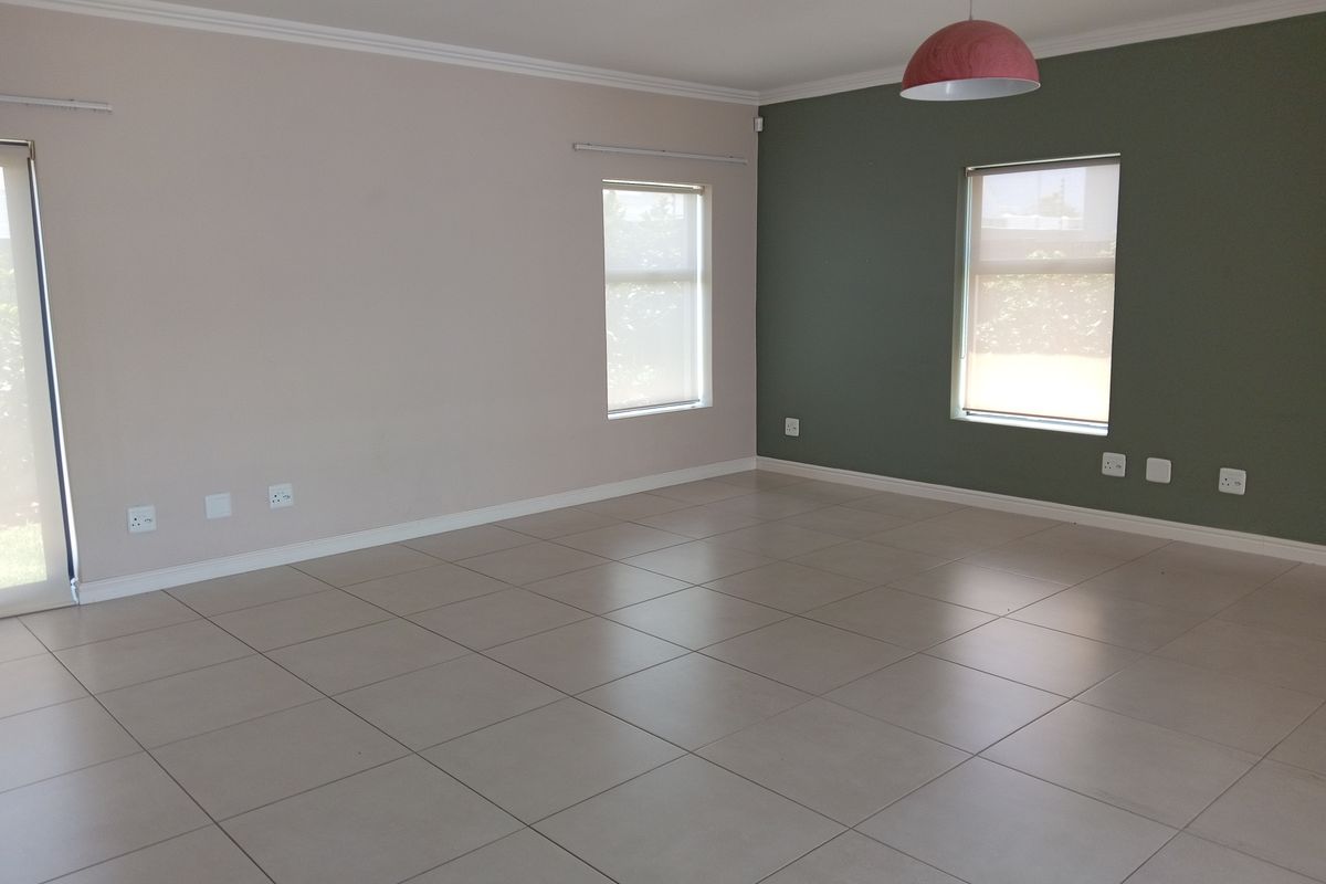 A spacious, empty living area featuring neutral tiled flooring, modern accent wall, and natural light through sliding doors and windows.