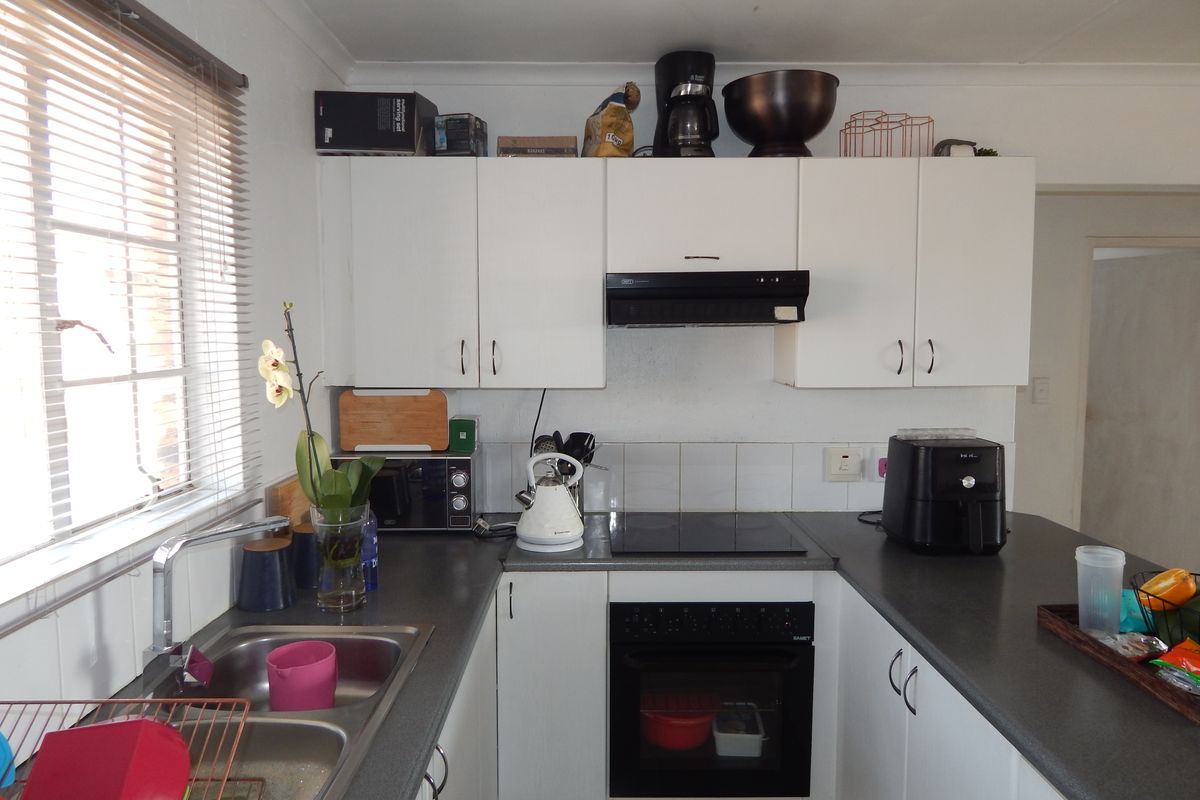 Functional kitchen featuring white cabinetry, dark laminate countertops, integrated oven and hob, and a stainless steel double sink with a window view.