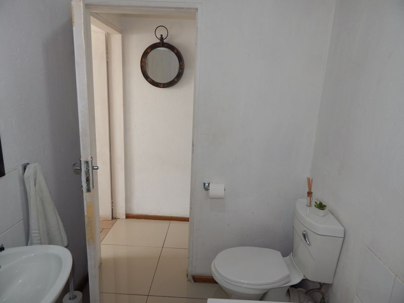 A functional bathroom featuring a standard toilet and washbasin with tiled flooring, requiring minor cosmetic updates to improve its overall appearance.