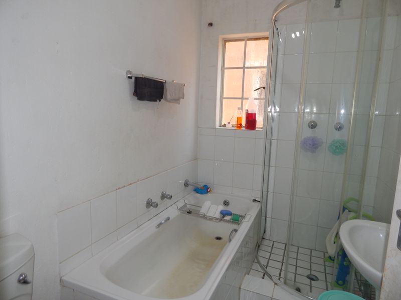 A functional bathroom featuring a bathtub, separate shower enclosure, pedestal basin, and toilet, with white tiled finishes throughout.