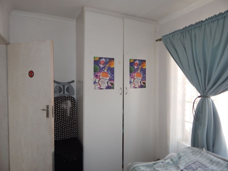 A bedroom featuring a white built-in wardrobe with double doors and a window with curtains.