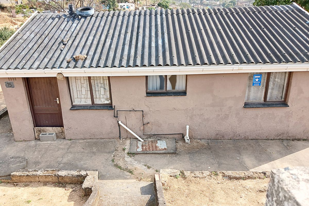 Rear exterior view of a single-story house featuring a corrugated roof, security bars on windows, and concrete stairs leading to the building.