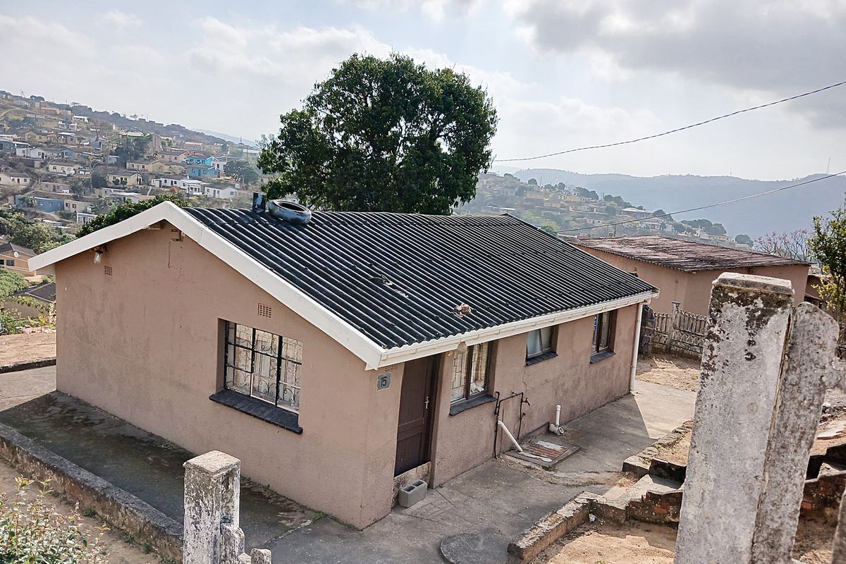 A detached single-story house featuring a corrugated roof, security bars on windows, and a concrete driveway in a residential neighborhood.