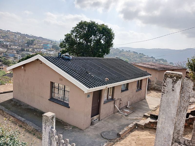 A detached single-story house featuring a corrugated roof, security bars on windows, and a concrete driveway in a residential neighborhood.