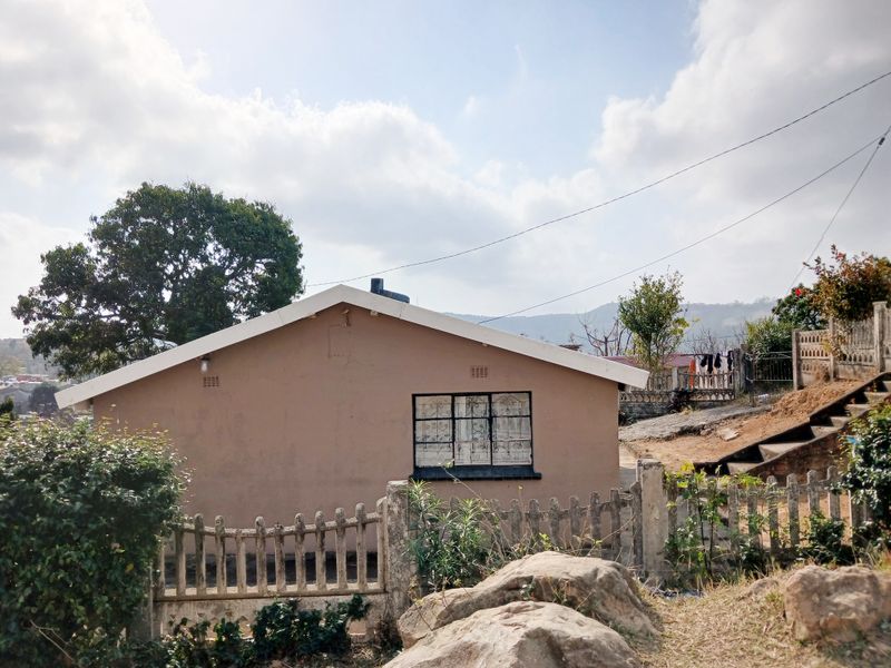 Rear view of the property showing the exterior wall, security-barred window, and concrete perimeter fencing on a sloped lot.