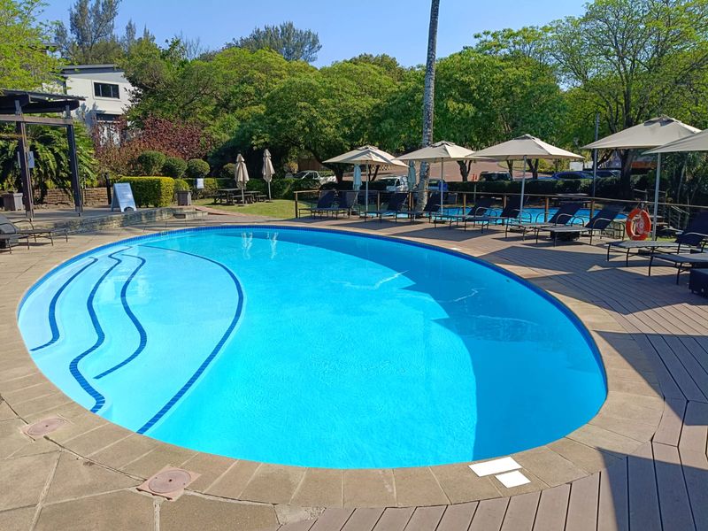 A well-maintained outdoor swimming pool area featuring paved and decked surrounds, set within a landscaped garden environment.