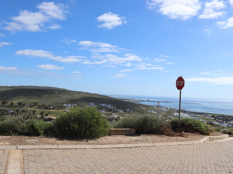 A street view looking out over the coastal landscape and surrounding residential area from a paved road.