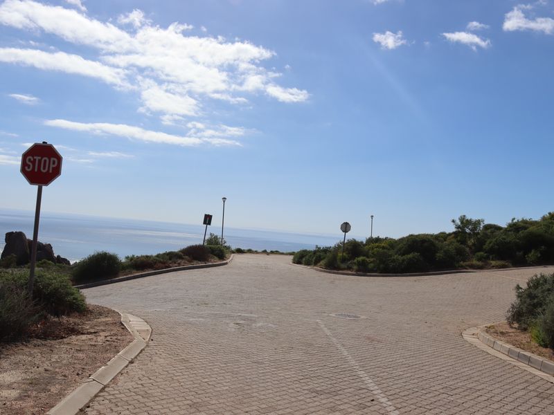 A paved residential street approach featuring kerbing and street lighting, offering an elevated view of the coastline.
