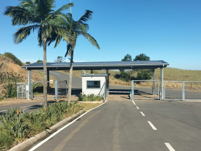 A secure estate entrance featuring a modern gatehouse, boom gate access control, perimeter fencing, and solar-powered roof infrastructure.