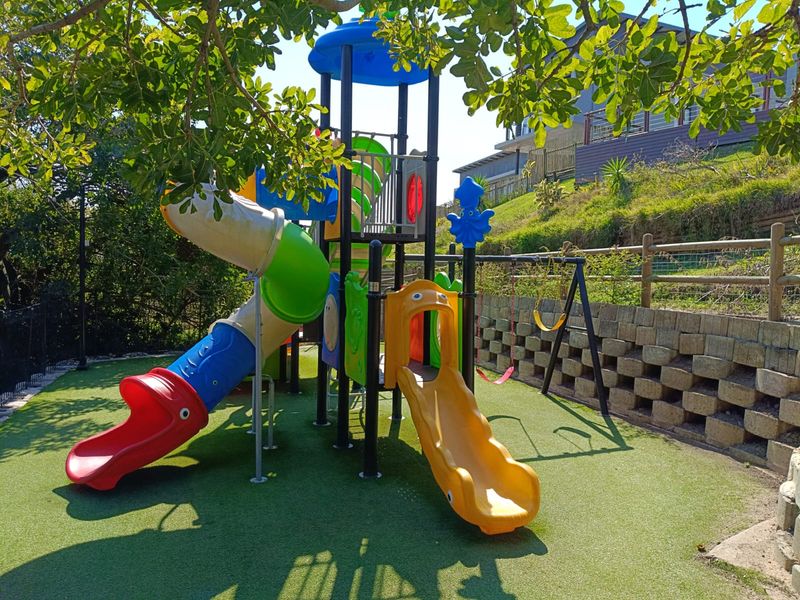 A well-maintained communal garden area featuring a children's playground structure, artificial turf, and a tiered retaining wall.