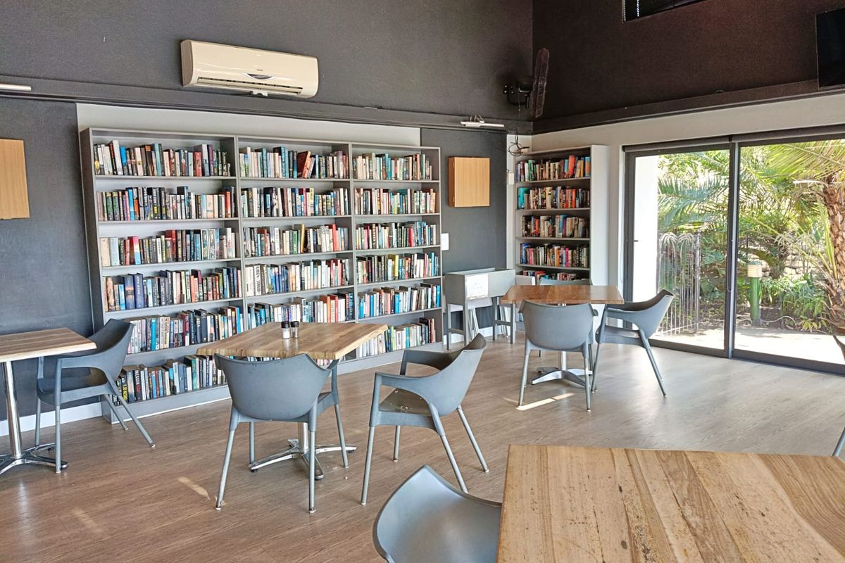 A spacious living area featuring extensive built-in bookshelves, laminate flooring, and large sliding glass doors providing natural light and garden access.