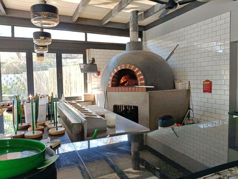 Covered outdoor entertainment area featuring a built-in wood-fired pizza oven, granite prep counters, and subway tile finishes with folding glass doors.