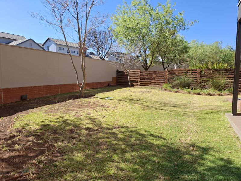 A private rear garden featuring a lawn, mature trees, and a combination of masonry boundary walls and timber fencing.