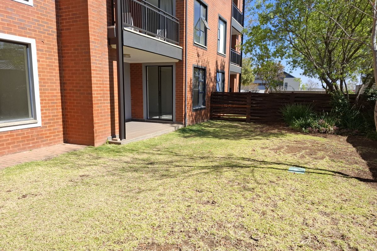 Rear view of a brick townhouse featuring a ground-floor patio, balcony above, and a private garden area with timber fencing.