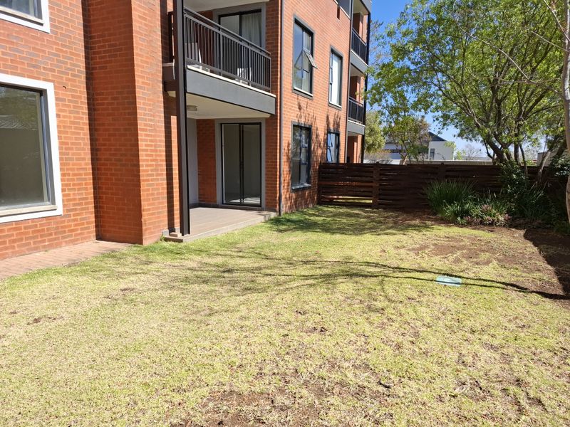 Rear view of a brick townhouse featuring a ground-floor patio, balcony above, and a private garden area with timber fencing.
