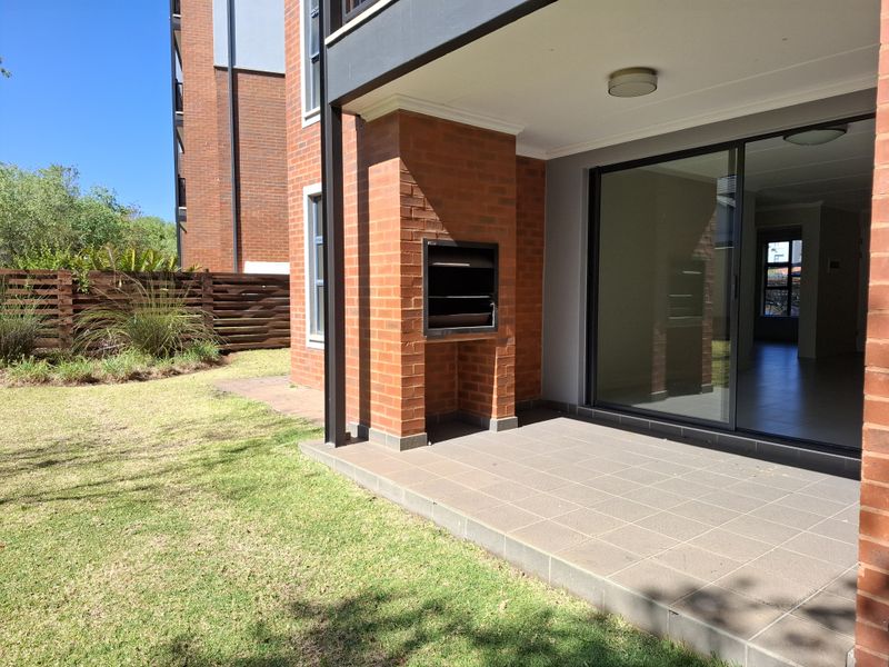 Covered patio featuring a built-in braai, tiled flooring, and sliding glass doors providing seamless access to the private garden area.