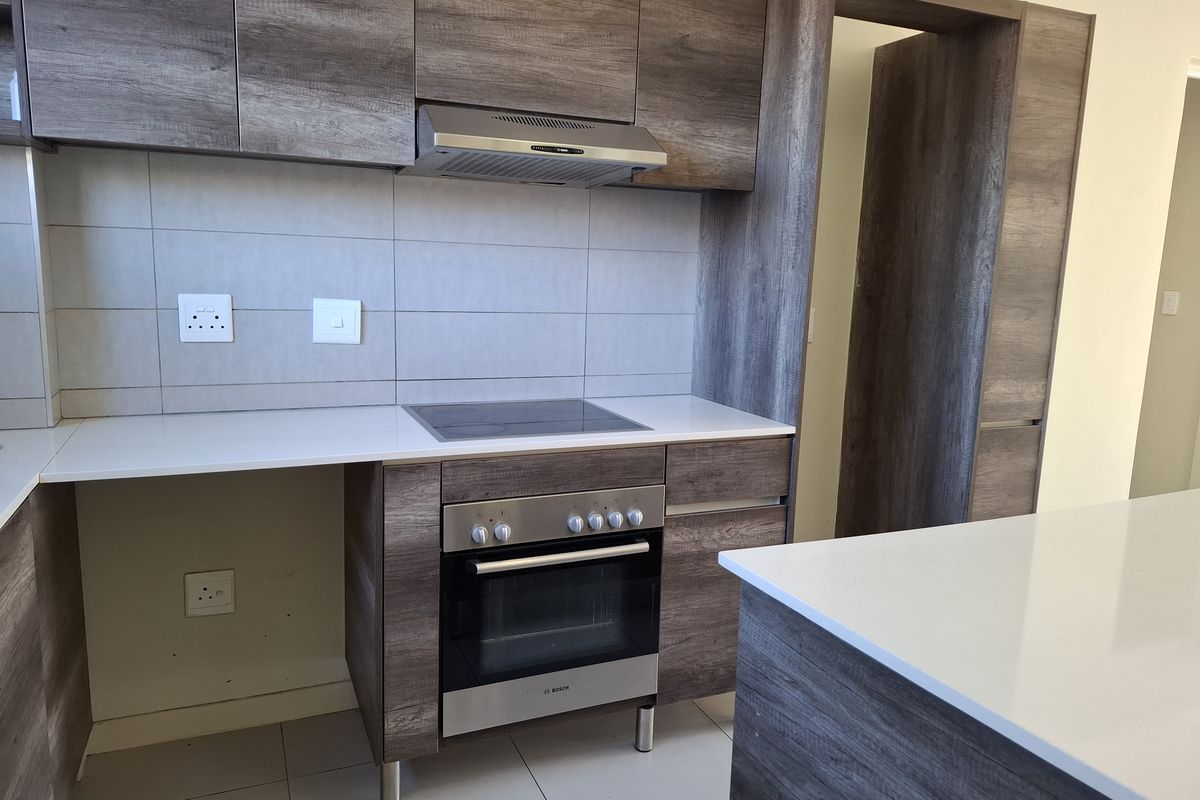 Modern kitchen featuring wood-grain cabinetry, stone countertops, integrated electric hob, oven, and extractor fan with a clean tiled backsplash.
