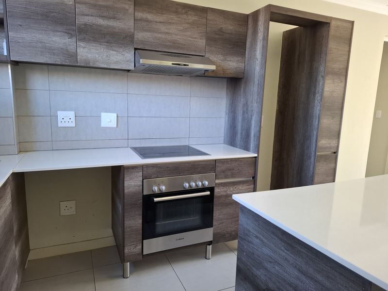Modern kitchen featuring wood-grain cabinetry, stone countertops, integrated electric hob, oven, and extractor fan with a clean tiled backsplash.