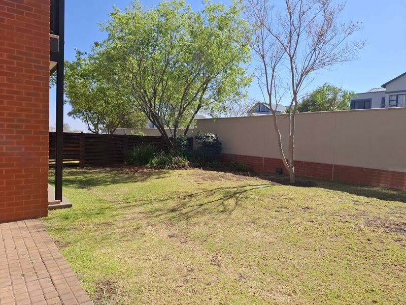 A private rear garden featuring a lawn area, brick paved patio section, and secure boundary walls with timber fencing.
