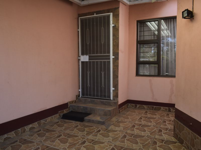 A covered patio area featuring tiled flooring, a security gate, and an external wall light, showing signs of wear on the exterior walls.